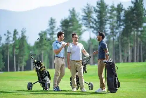 Three friends laughing on golf course with golf clubs